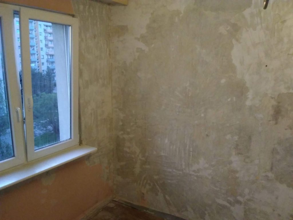 Ściana z nierówną powierzchnią obok okna w pomieszczeniu podczas remontu.