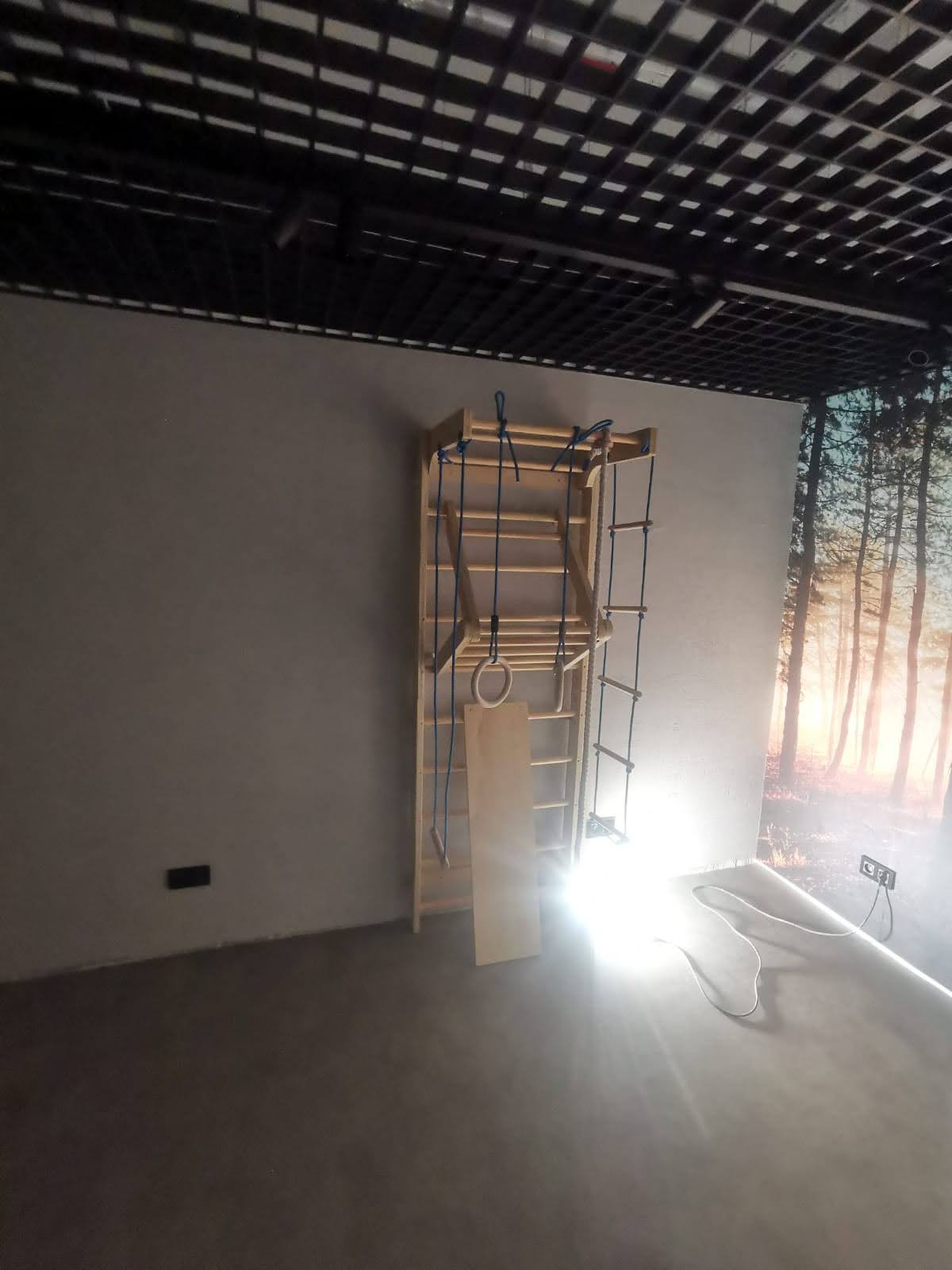 Drabina przy ścianie pod czarnym sufitem kratowym.