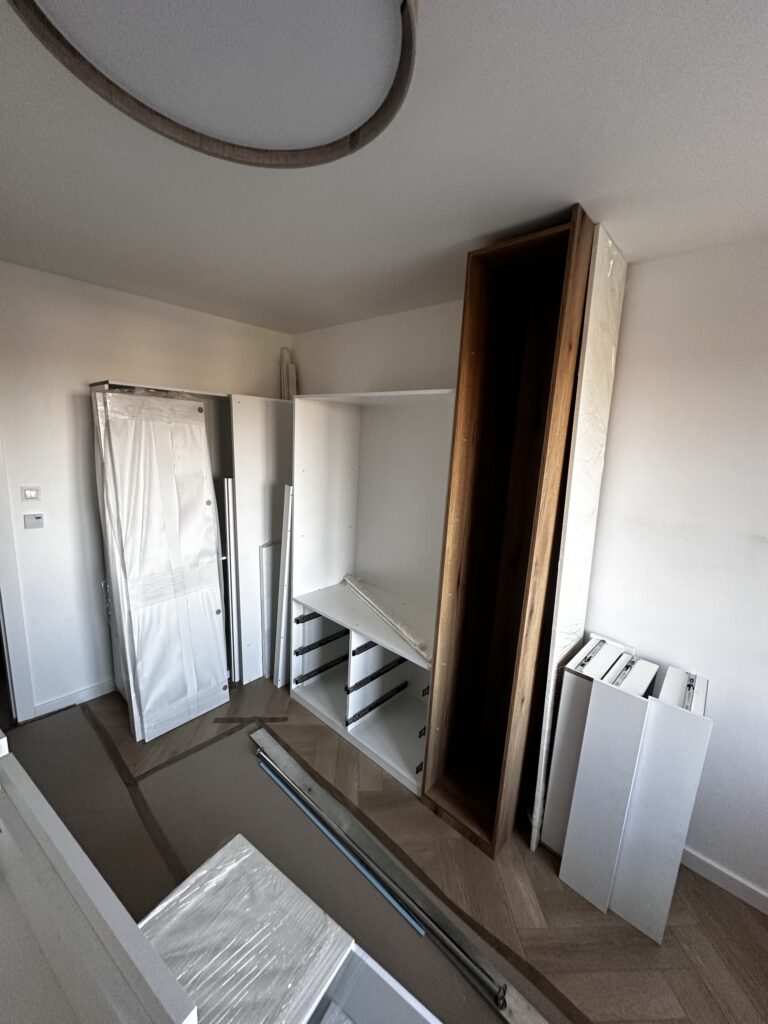 Montaż mebli w pomieszczeniu z lustrzanymi frontami i otwartymi półkami.