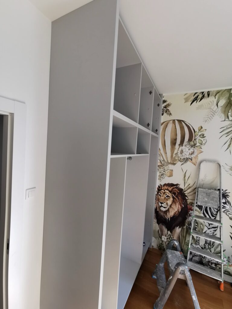 Otwarty korpus białej szafy podczas montażu obok drabiny
