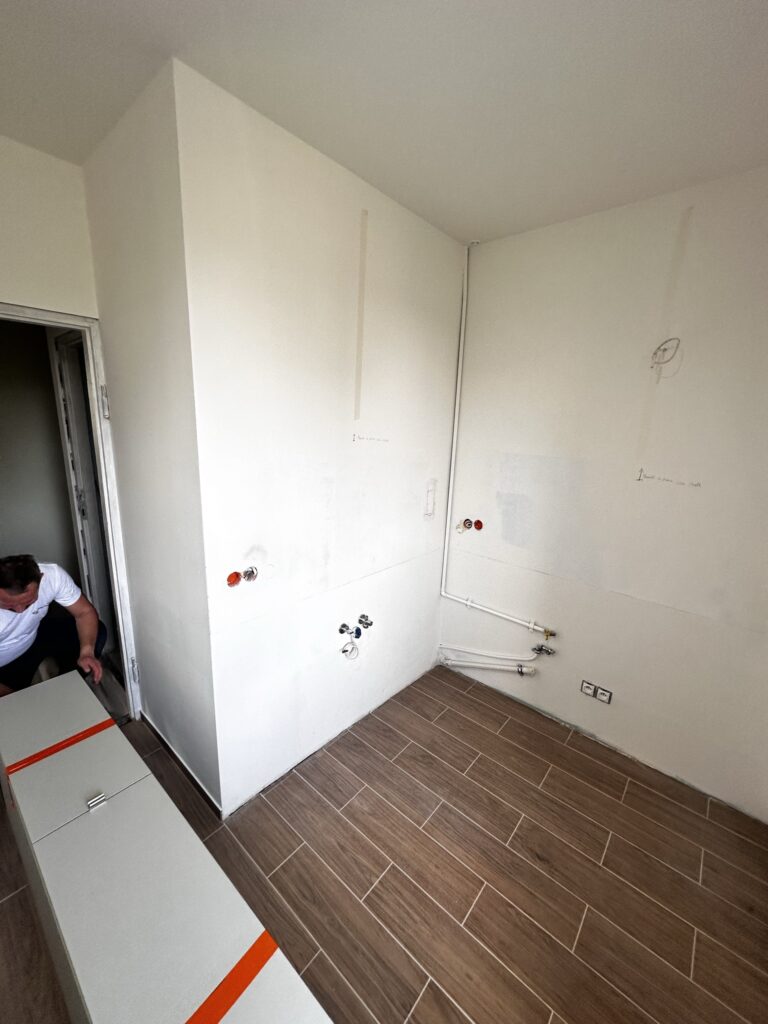 Jasne pomieszczenie z drewnianą podłogą i punktami instalacyjnymi.