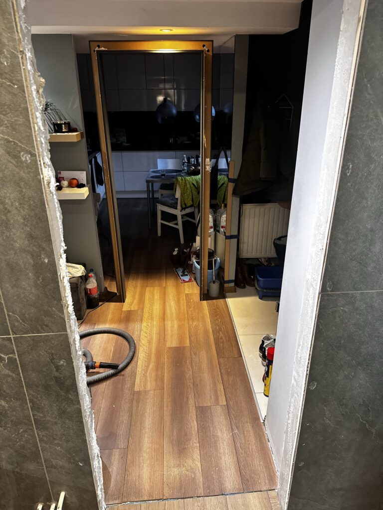 Wąski korytarz z drewnianą podłogą podczas prac wykończeniowych.