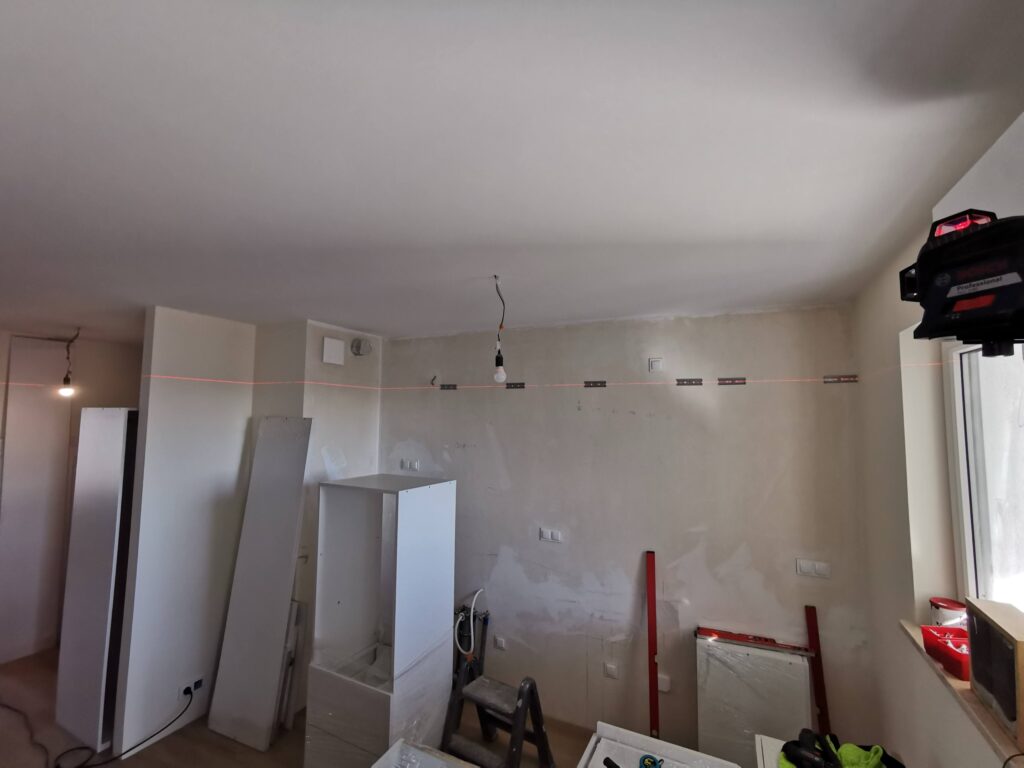 Remontowane wnętrze z białymi szafkami, drabiną i materiałami budowlanymi