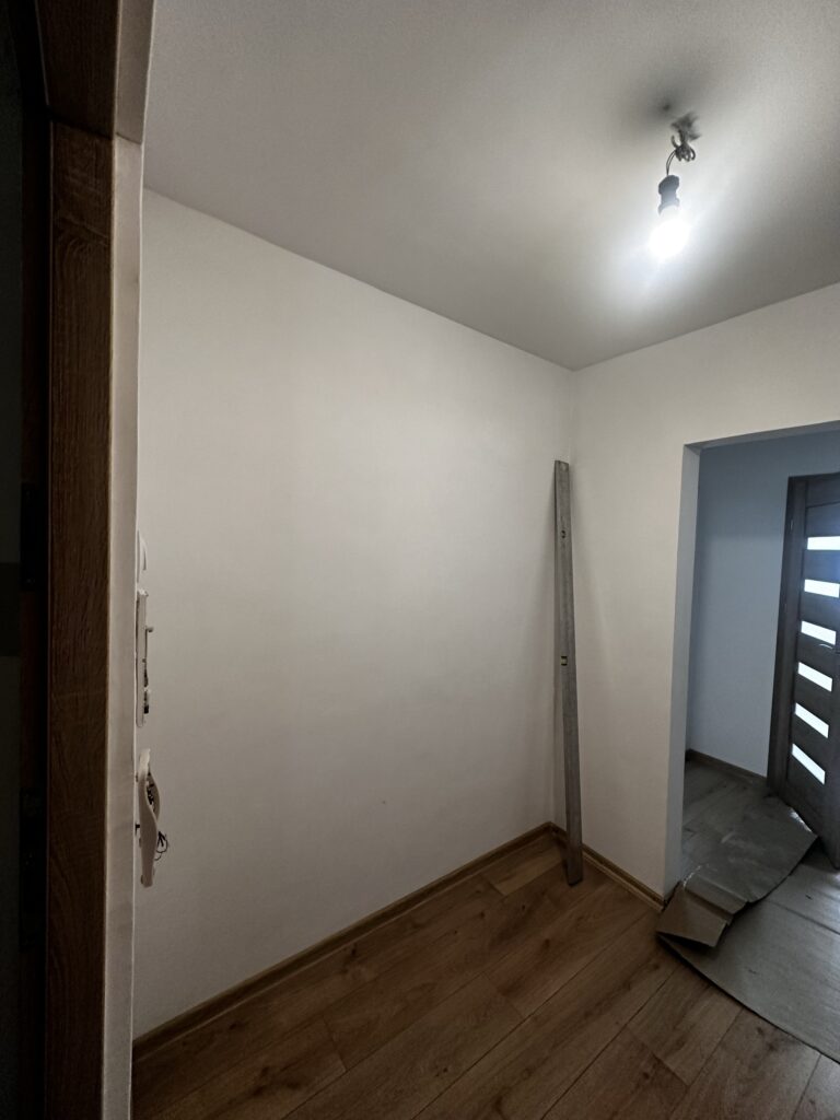 Pusty korytarz z drewnianą podłogą przy drzwiach wejściowych.