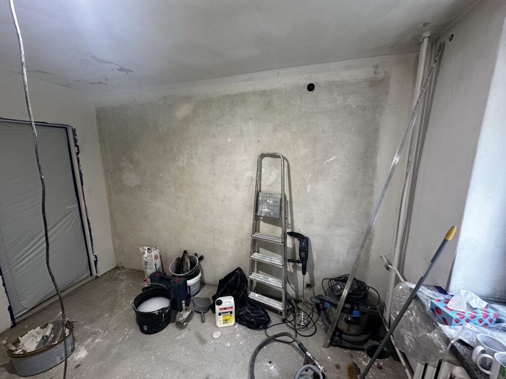 Pomieszczenie w remoncie z drabiną i narzędziami na podłodze.