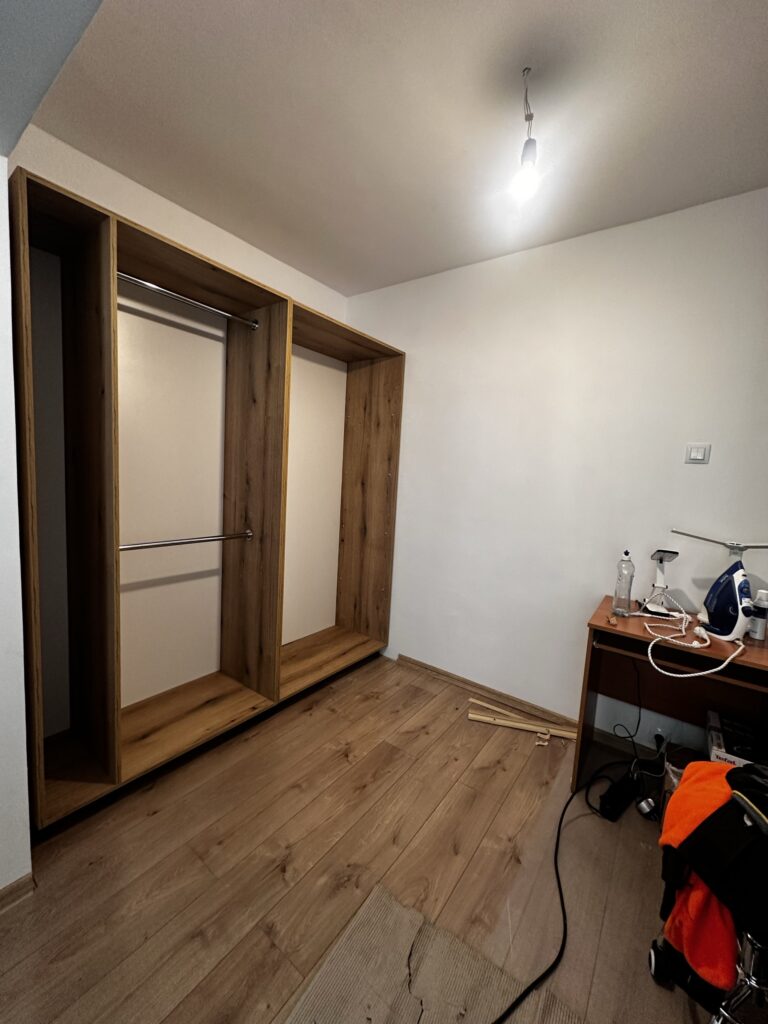 Pokój z drewnianą podłogą i montowaną szafą wnękową.