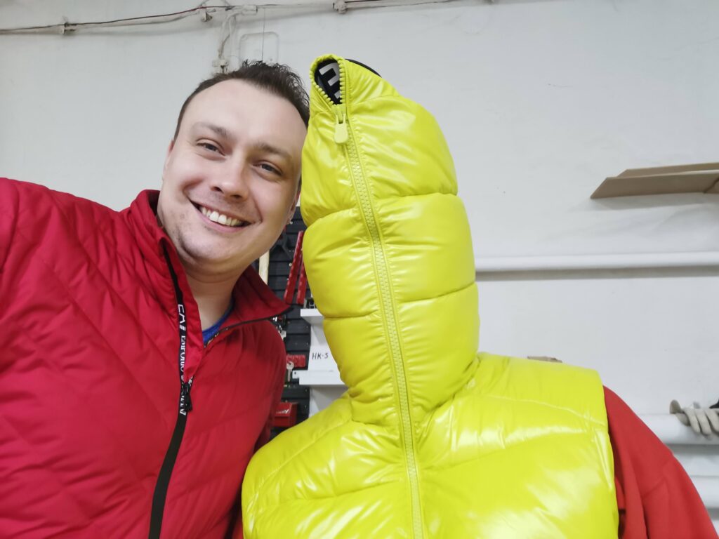 Mężczyzna w czerwonej bluzie obok żółtej puchowej kurtki na manekinie.