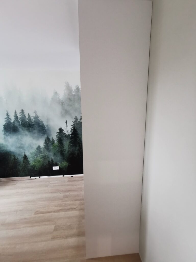 Boczny widok wysokiej białej szafy obok leśnej fototapety