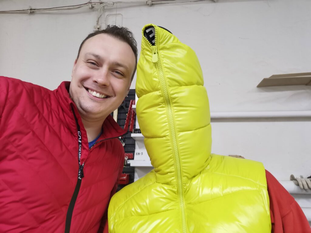 Mężczyzna w czerwonej bluzie obok żółtej puchowej kurtki na manekinie.