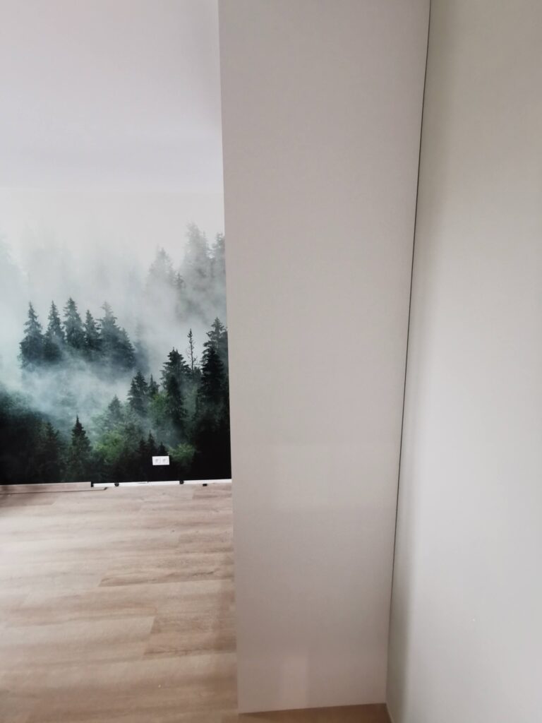 Wysoka biała szafa stojąca przy ścianie z leśną fototapetą