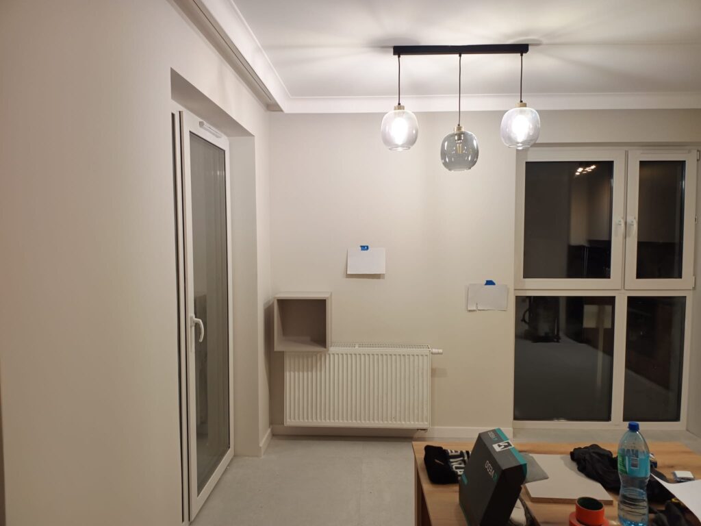 Jasne wnętrze z lampami wiszącymi, kuchennym blatem i wejściem do korytarza.