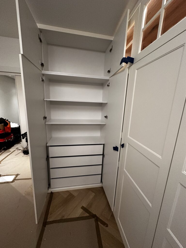 Otwarta biała szafa z półkami i szufladami.