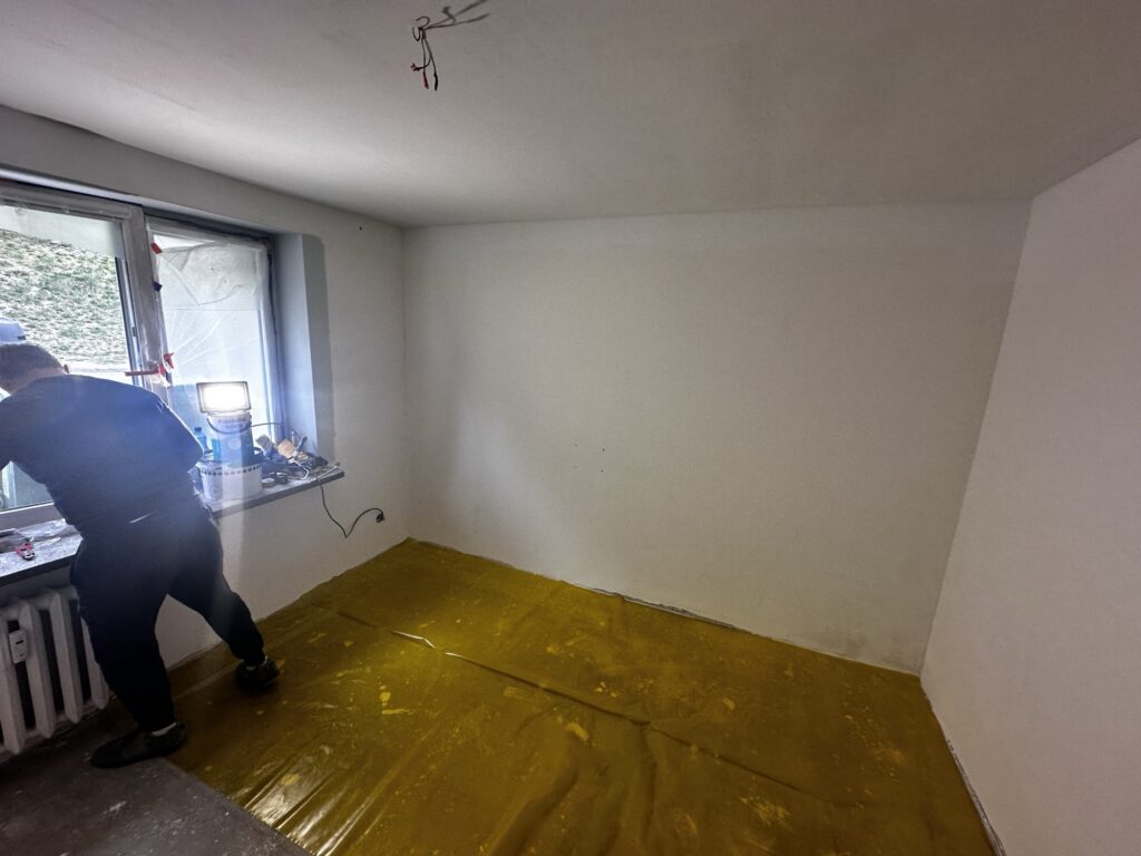 Pomieszczenie w trakcie remontu z żółtą folią ochronną na podłodze.