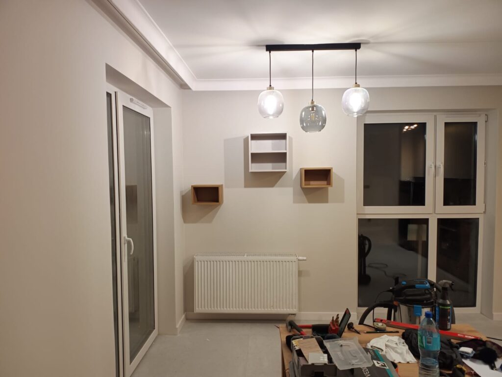 Jadalnia z lampami wiszącymi, grzejnikiem i pudełkami na podłodze.
