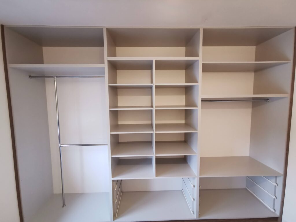 Wnętrze białej szafy z półkami, drążkami i prowadnicami szuflad