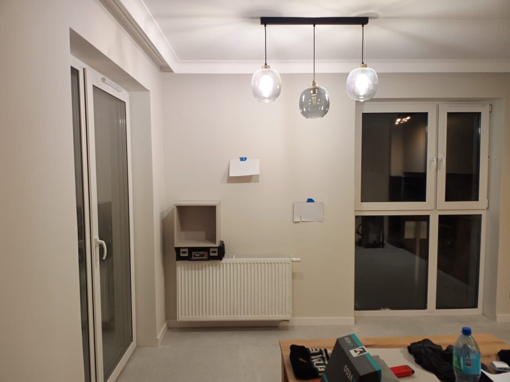 Jadalnia z lampami wiszącymi, grzejnikiem i drzwiami balkonowymi.