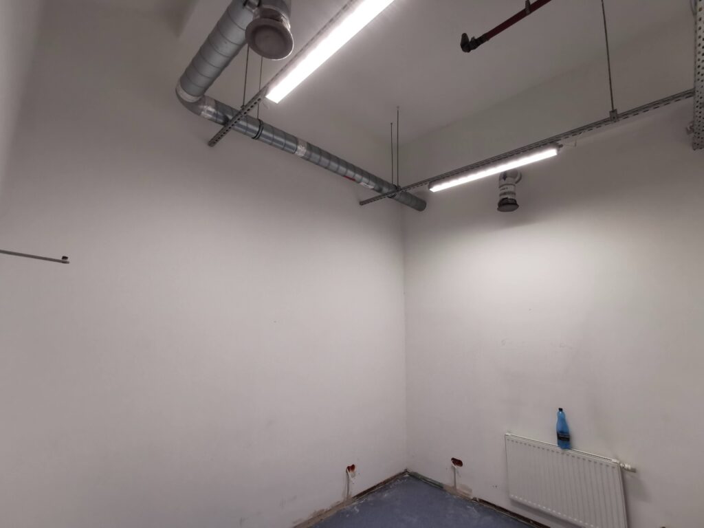 Białe pomieszczenie z instalacją pod sufitem i lampami.