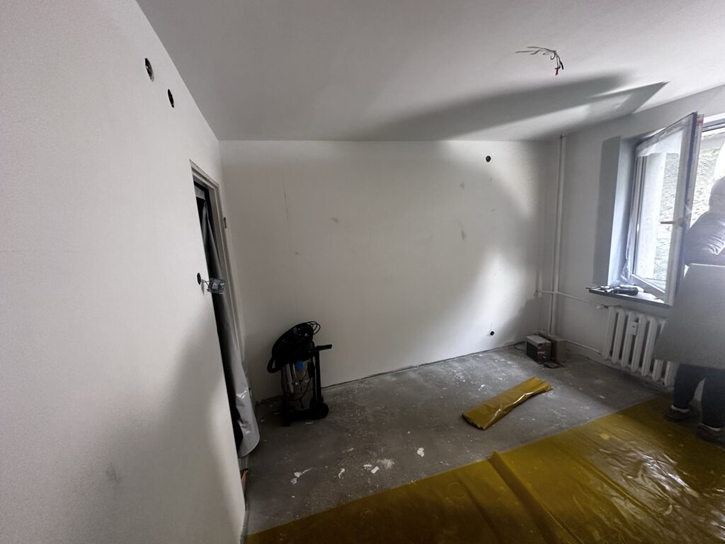 Pusty pokój w trakcie remontu z żółtą folią ochronną na podłodze.