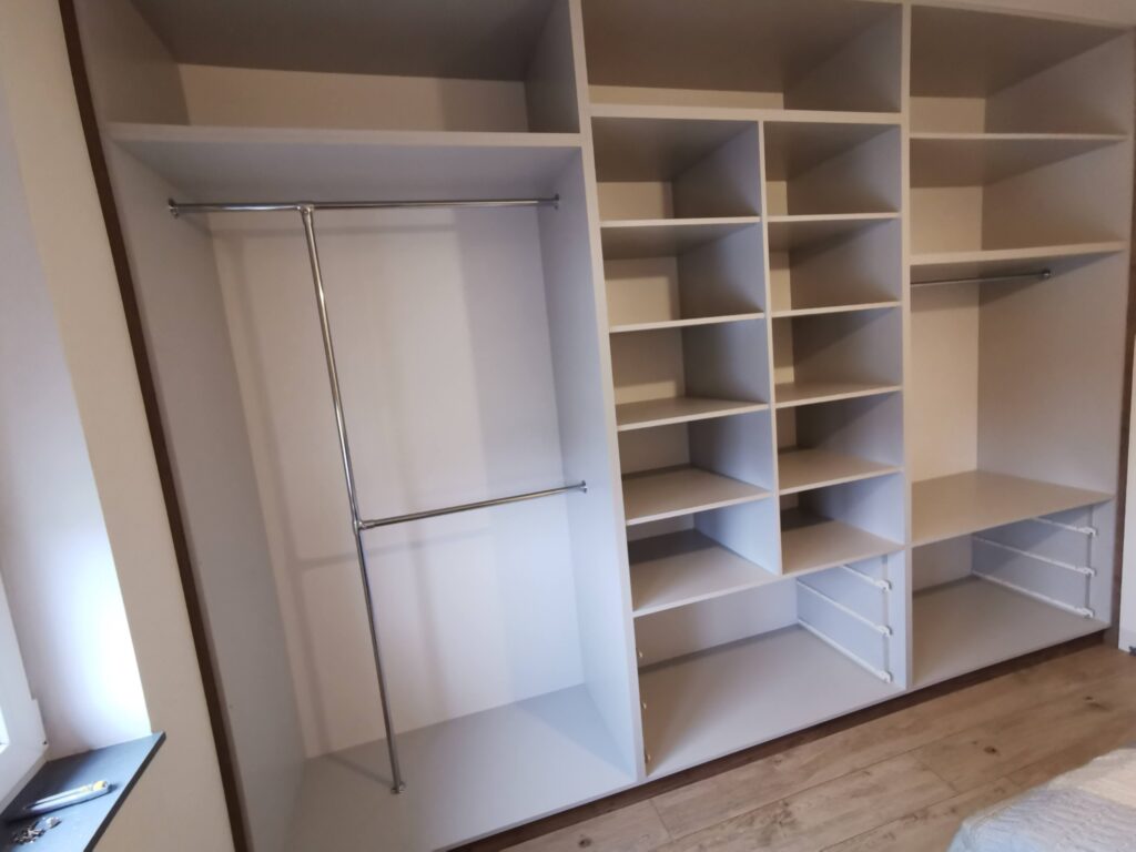 Wnętrze dużej szafy z licznymi półkami, drążkami i szufladami