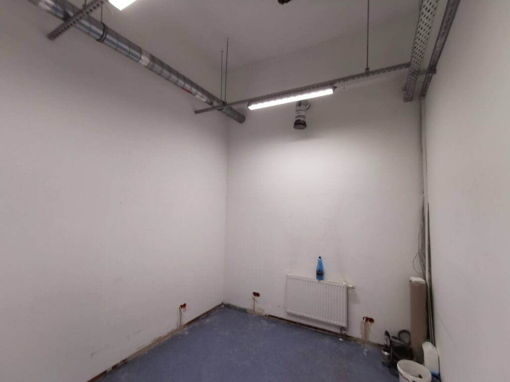 Niewykończone pomieszczenie z niebieską podłogą i instalacją sufitową.