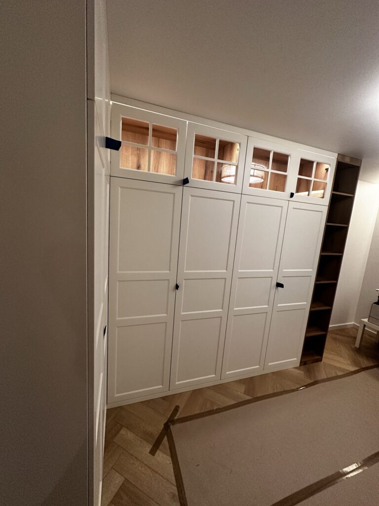 Biała zabudowa szaf z przeszklonymi górnymi segmentami.