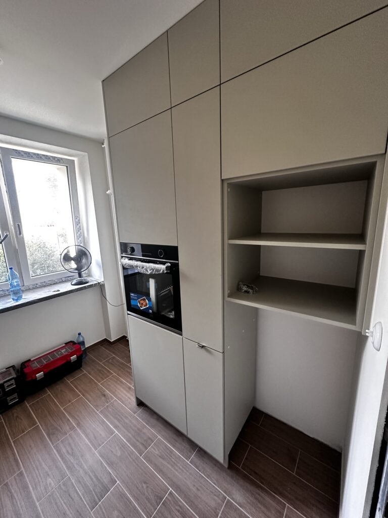 Jasna szafa z wnęką i półkami przy oknie.