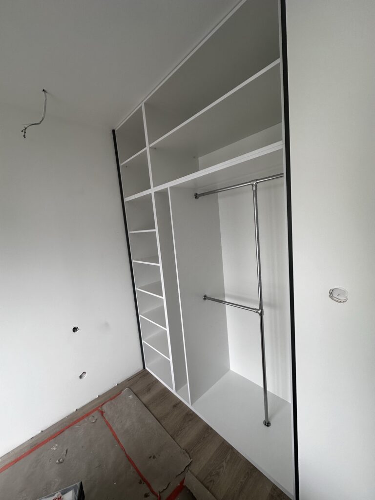 Otwarta szafa wnękowa z półkami i drążkiem.