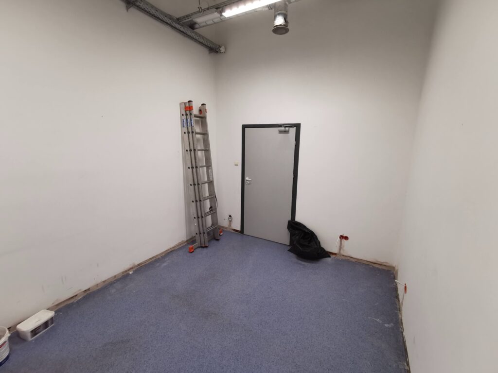 Puste białe pomieszczenie z drabiną, drzwiami i niebieską podłogą.
