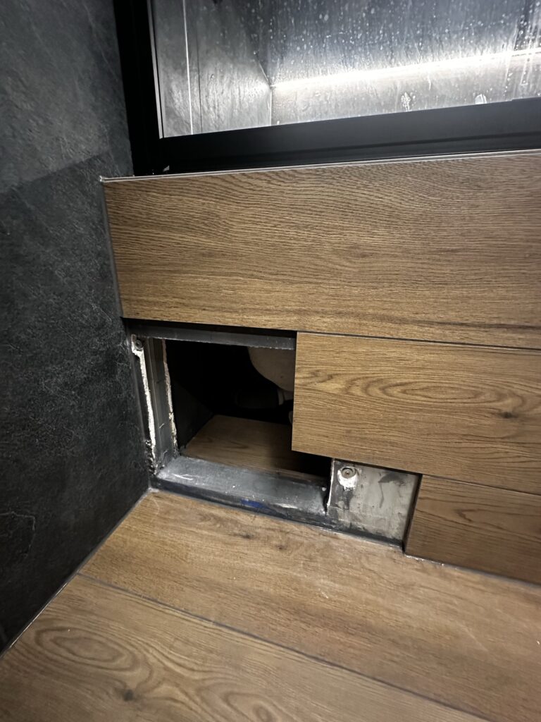 Drewniana zabudowa z otworem serwisowym pod umywalką.
