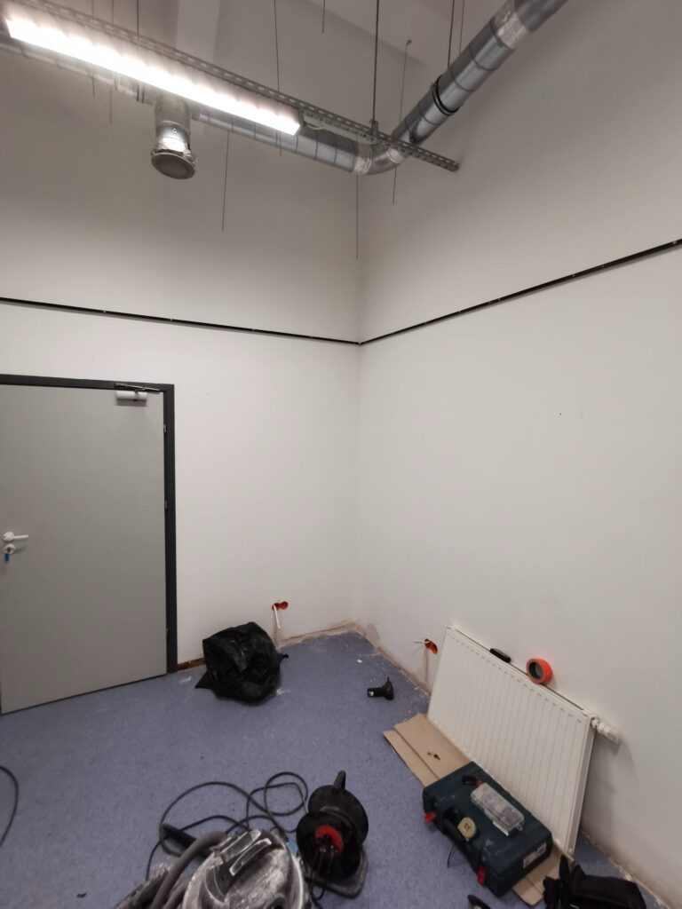 Białe pomieszczenie z narzędziami i metalową konstrukcją pod sufitem.