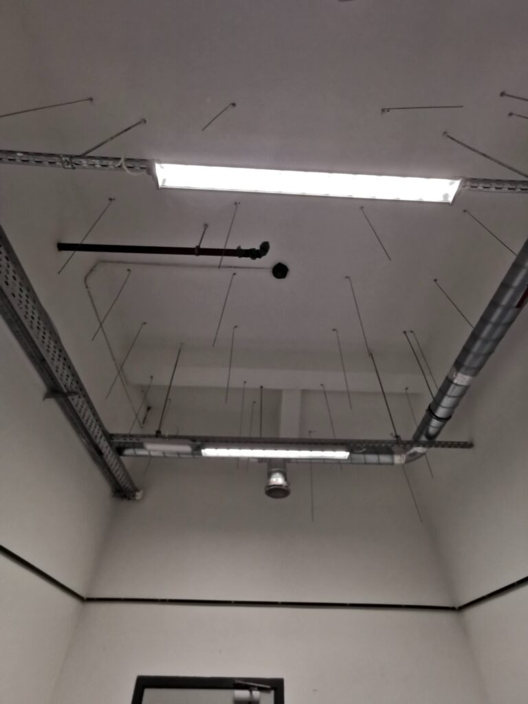 Sufit z widocznymi instalacjami i lampą.