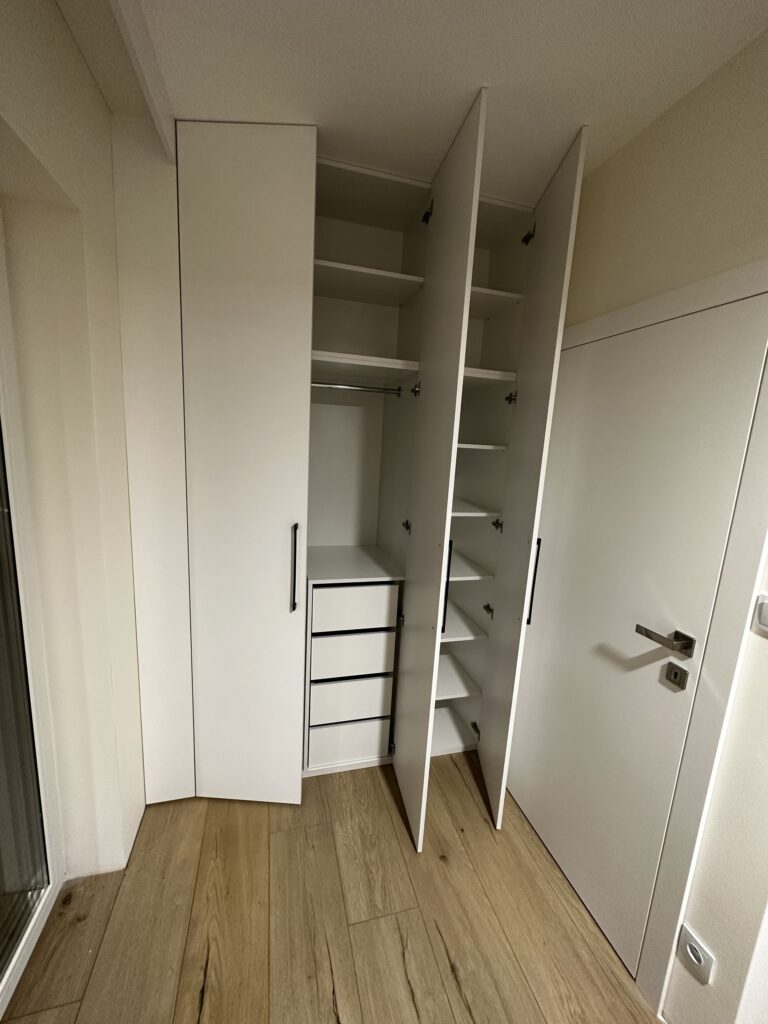 Otwarta biała szafa z półkami i szufladami.