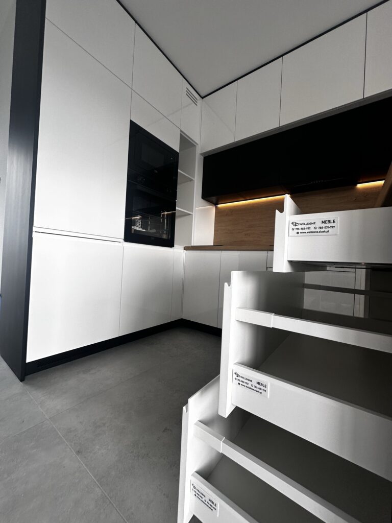 Otwarte szuflady w białej zabudowie kuchennej.