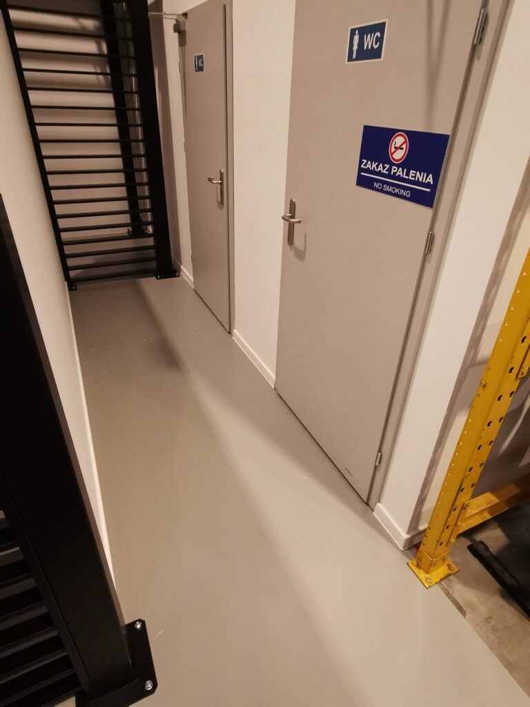 Białe drzwi techniczne obok czarnej ażurowej przegrody.