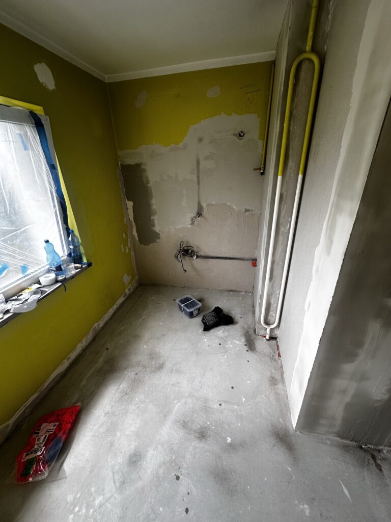 Pomieszczenie z surową podłogą i odkrytą instalacją.