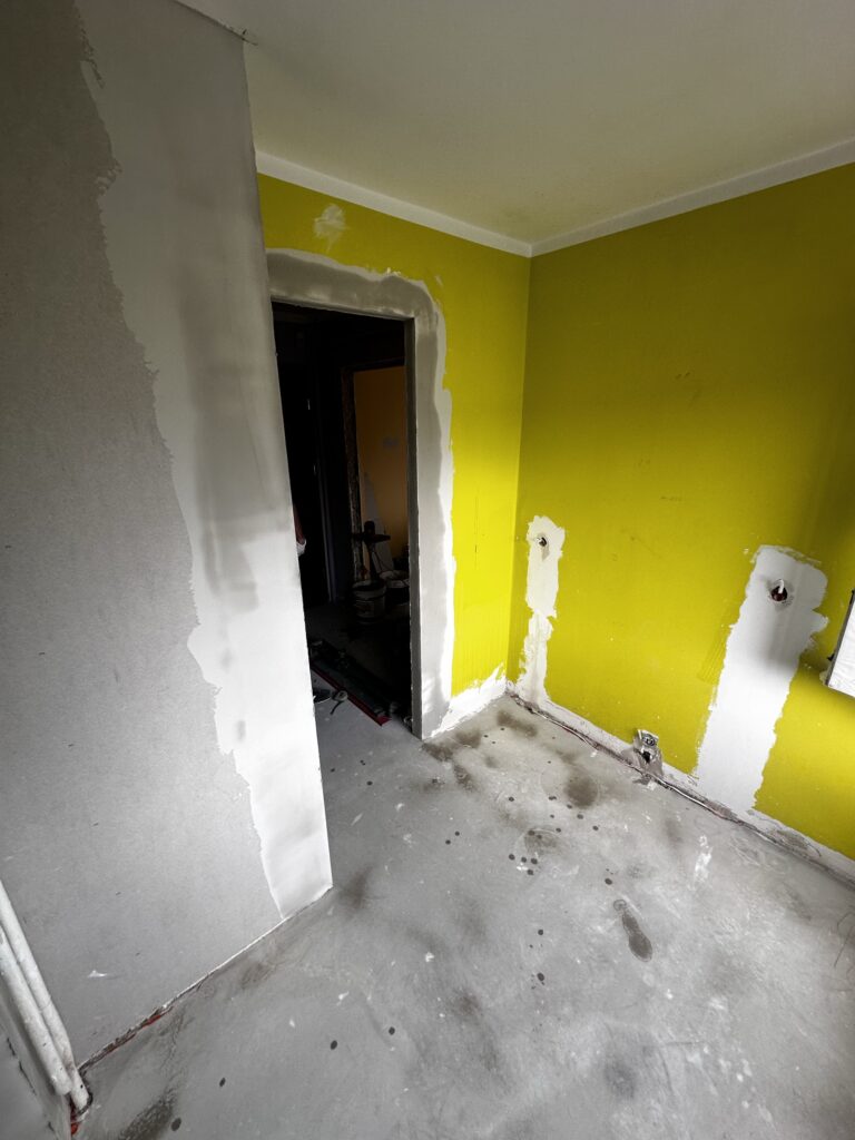 Remontowany pokój z żółtymi ścianami i odkrytą instalacją.