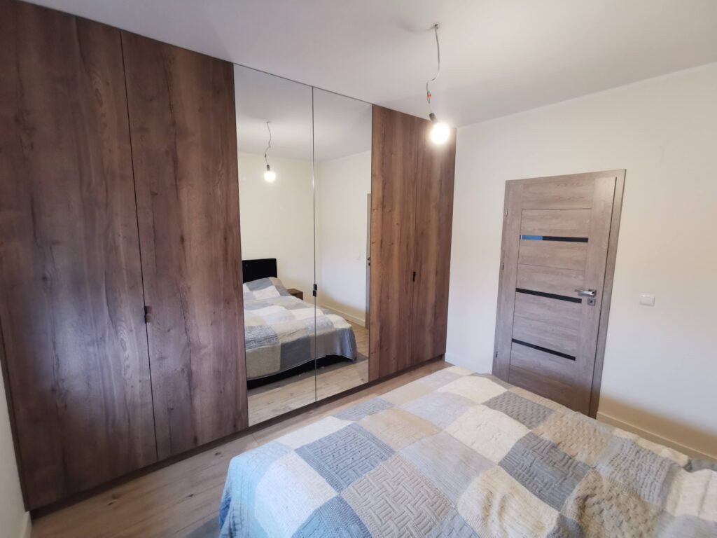 Drewniana szafa z lustrzanymi drzwiami stojąca naprzeciw łóżka