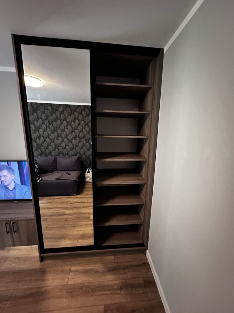Wysoka szafa z lustrem i otwartymi półkami.