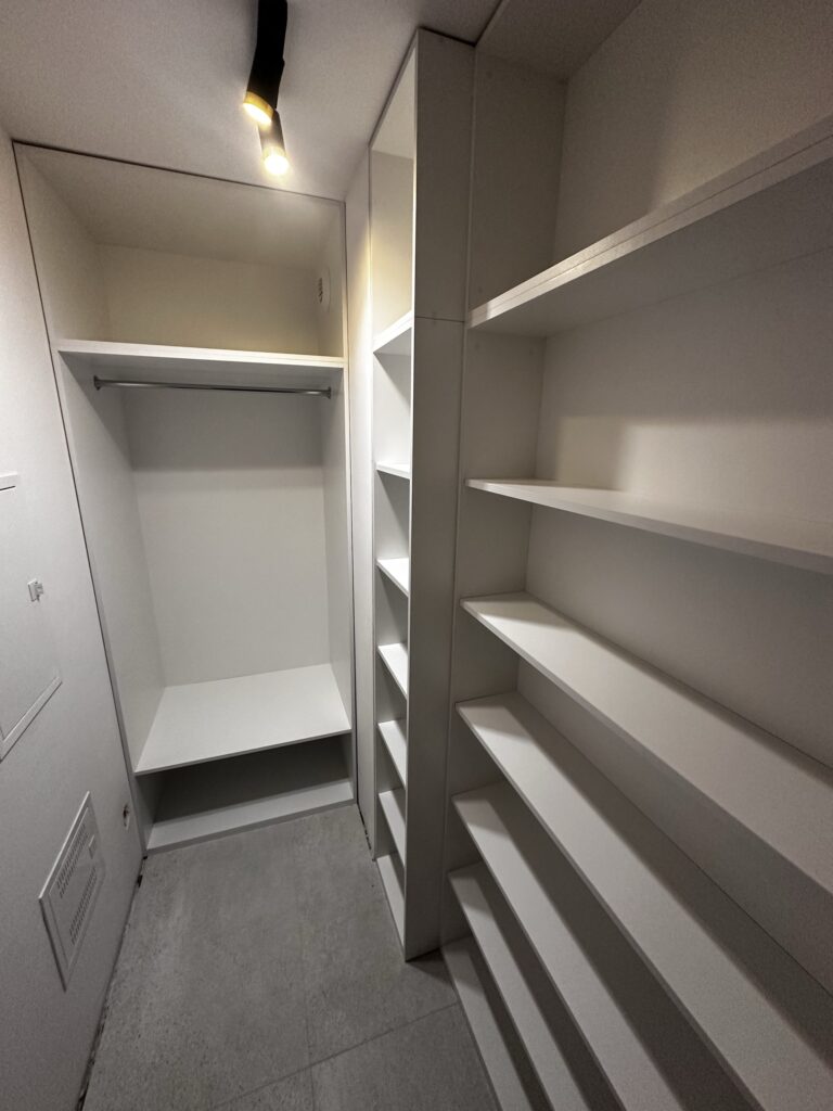 Otwarta biała garderoba z półkami i miejscem na ubrania.