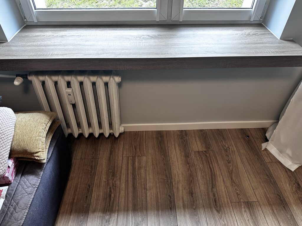 Drewniana podłoga przy oknie i grzejniku.