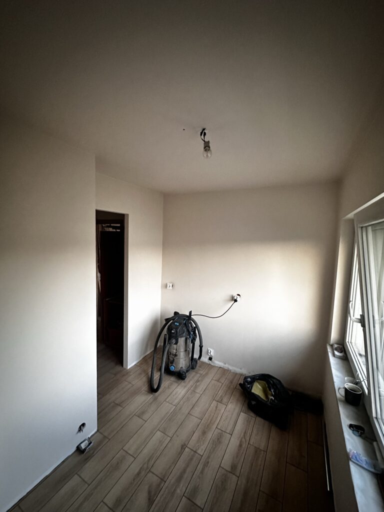 Pusty pokój z drewnianą podłogą i materiałami przy ścianie.