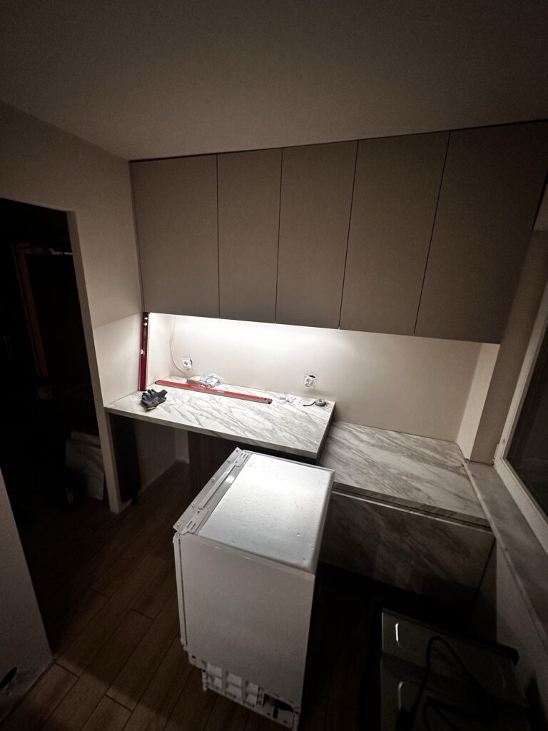Kuchnia w trakcie montażu z beżowymi szafkami i jasnym blatem.