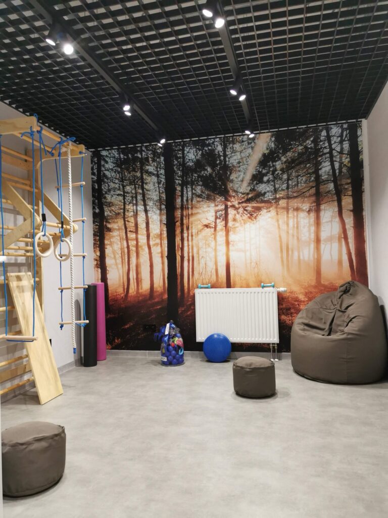 Pomieszczenie z leśną grafiką na ścianie i pufami.