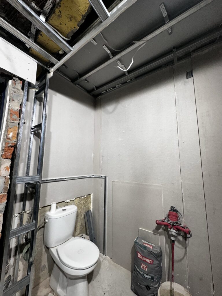 Remontowana toaleta z instalacjami pod sufitem.