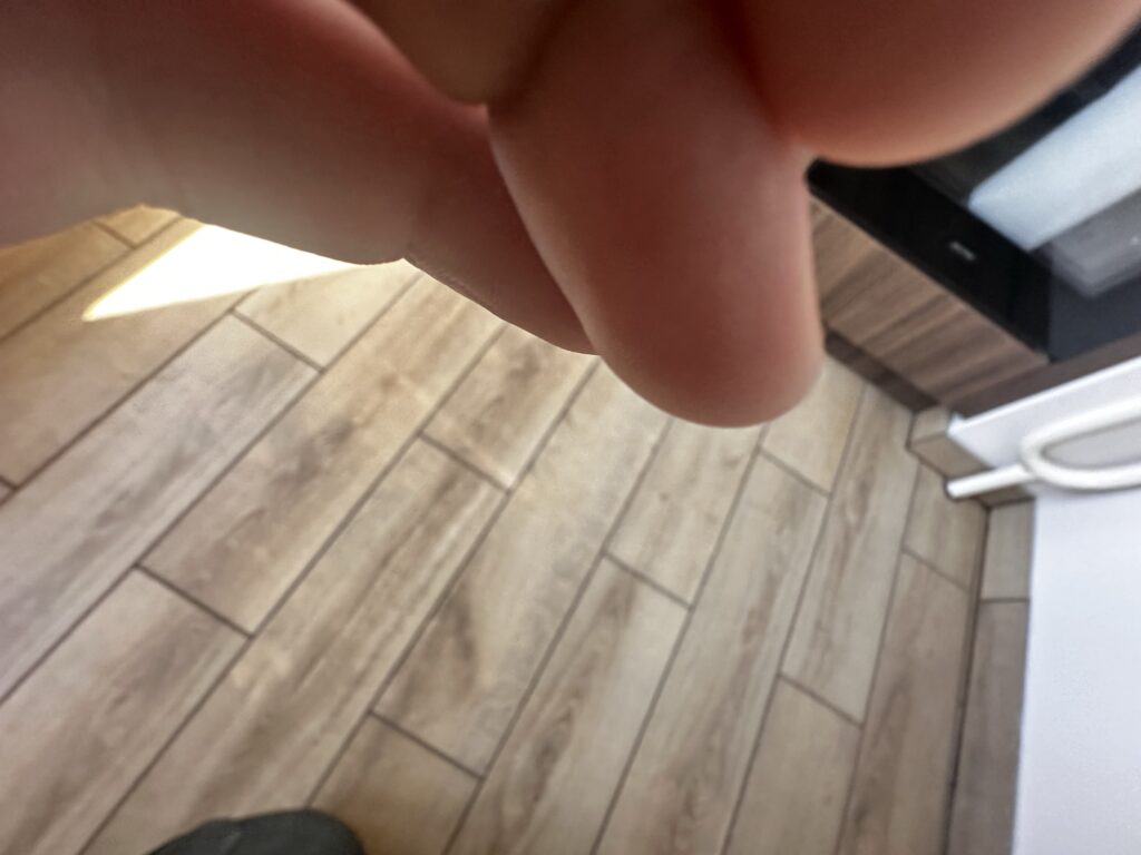Fragment drewnianej podłogi częściowo zasłonięty dłonią.