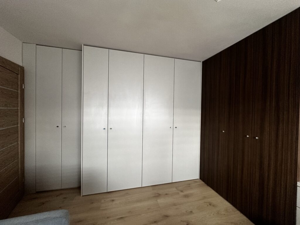 Biała szafa przy drewnianej ścianie w sypialni.