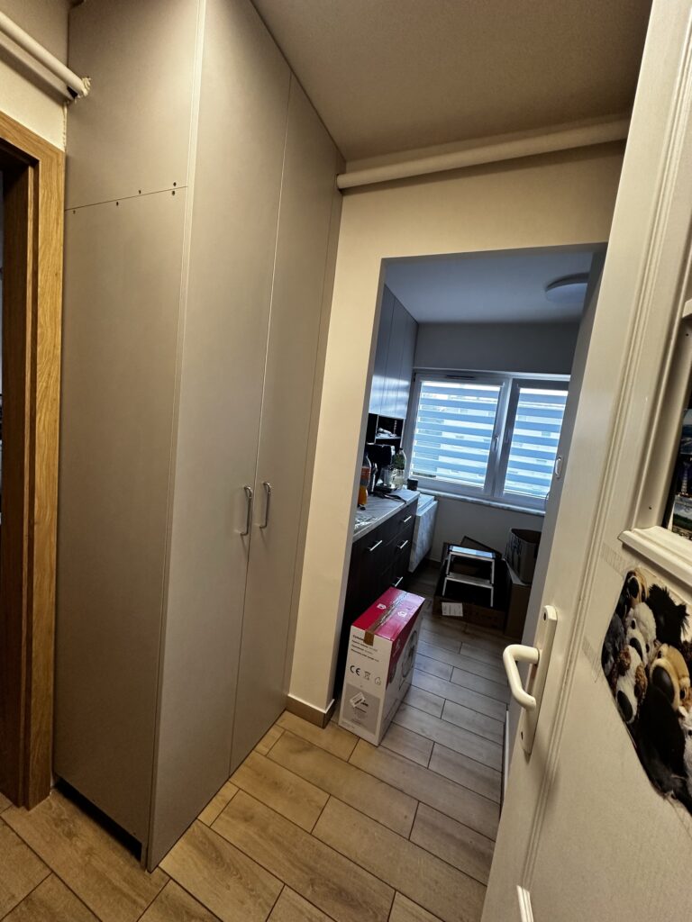 Wysoka biała szafa w korytarzu przy wejściu do pokoju.