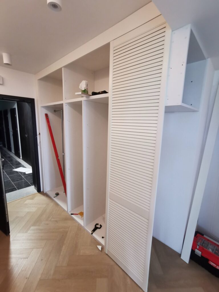 Otwarta biała szafa z półkami podczas montażu ażurowego frontu