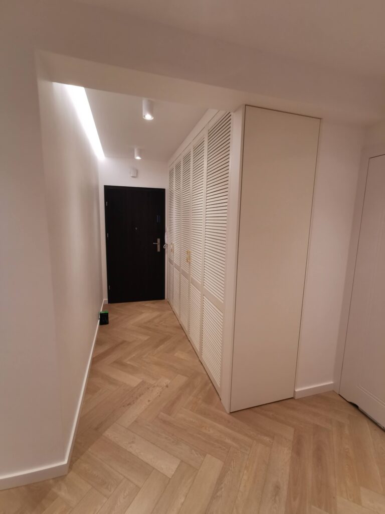 Biała szafa z lamelowymi drzwiami w jasnym korytarzu